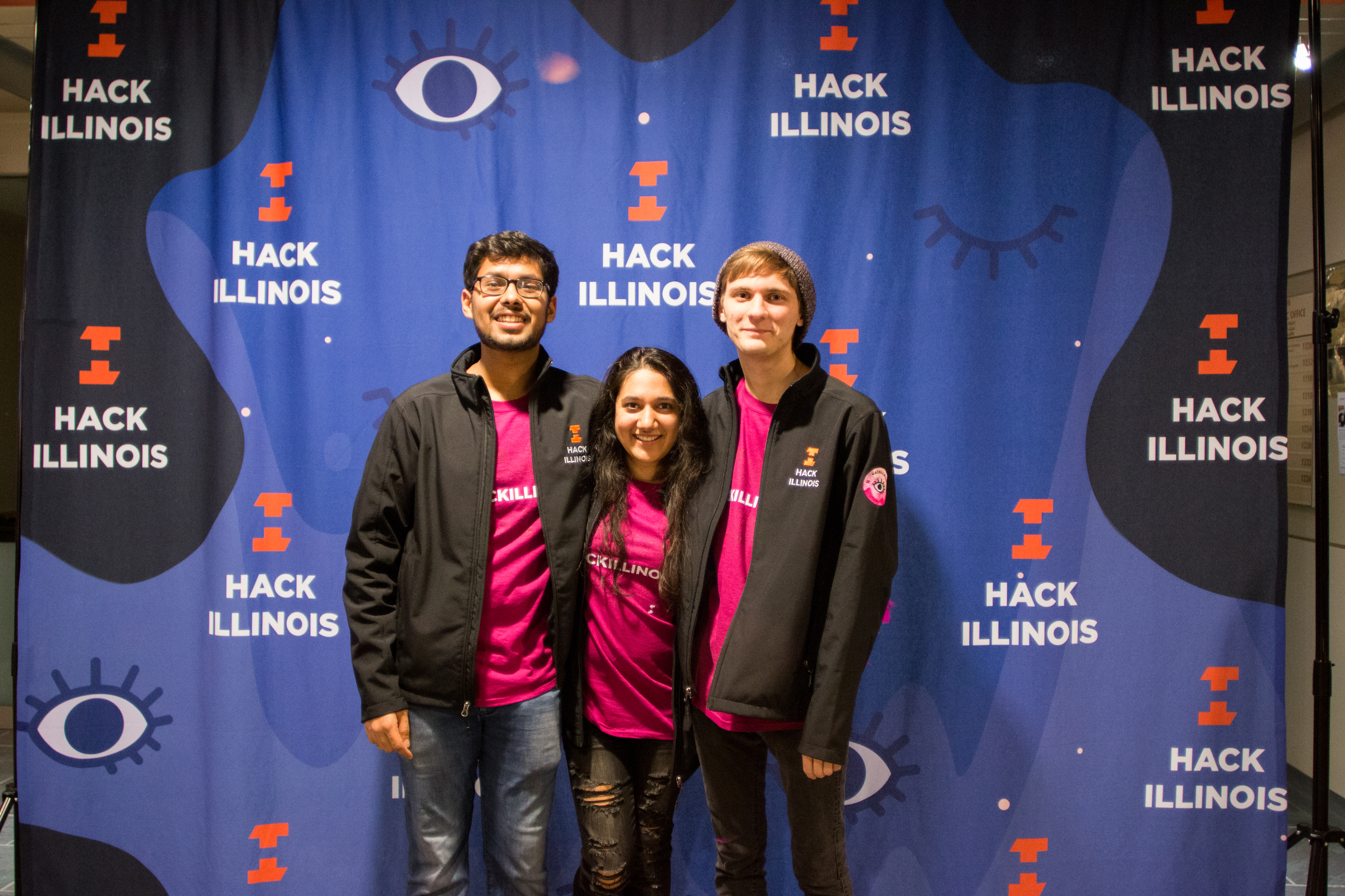 A group of HackIllinois 2018 staff members take a picture in front of the photobooth in their staff t-shirts and jackets.